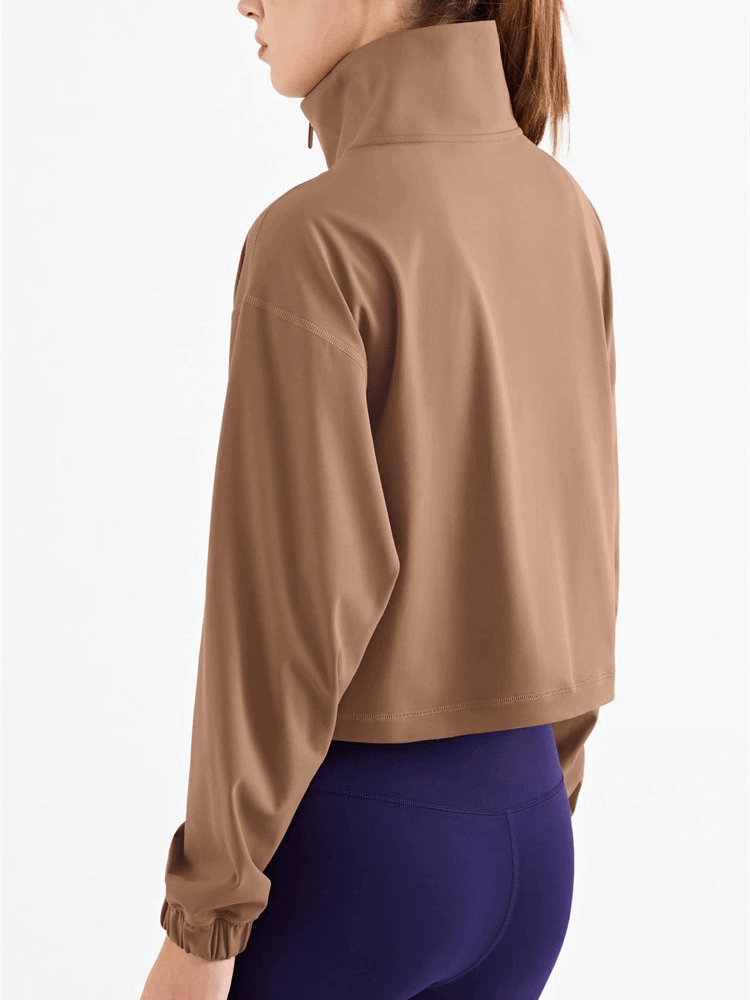 Woman wearing a brown workout sweatshirt with high collar and long sleeves, paired with purple leggings. Ideal for fitness enthusiasts.